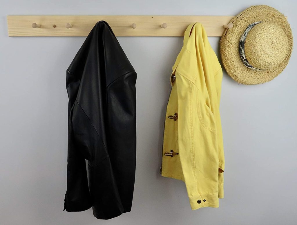 Natural wood peg rail, with a yellow and black coat hanging on it.